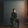 Man in a blazer sitting on a stool in front of a photography backdrop with studio lights on each side